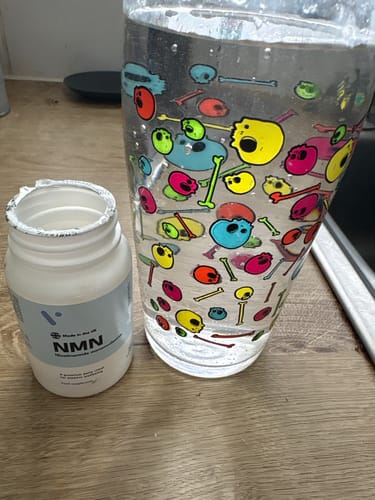 Flacon de complément Pure NMN de la cliente à côté d'un verre décoré de crânes et d'os colorés sur une surface en bois.