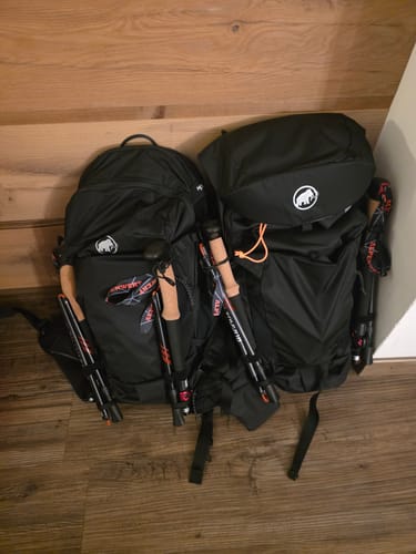 Reviewer's gefaltete Wanderstöcke Rugova Pro 3, befestigt an zwei Rucksäcken auf einem Holzboden.