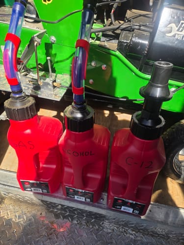Customer's three red 1.25 Gallon Jugs, two with hoses and one with a spout, labeled by hand on a trailer floor.