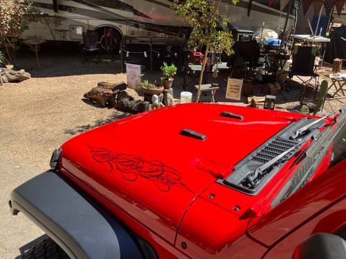 Customer's black custom vinyl decal applied to the hood of a red Jeep parked outdoors.