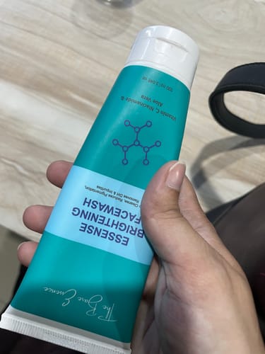 Customer's hand holding a turquoise and white Essense Deep Cleansing Facewash tube.
