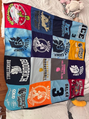 Customer's Project Repat T-Shirt Quilt featuring various colorful school sports and club logos on a white bedspread.