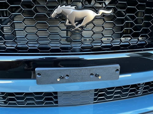 Customer's black number plate bracket mounted on the front bumper of a Ford Mustang.
