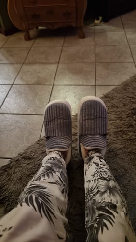 Customer's grijsgekleurde HappyComfy pantoffels gedragen op een vloer en kleed.