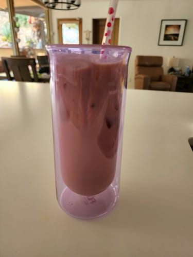 Customer's purple FLUR Iced Coffee Glass holding an iced drink with a straw on a counter.
