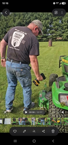 Reviewer's Turbo Jet DB v3.0 held in hand near a green riding lawnmower on a sunny day.
