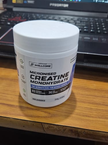 Customer's white tub of Wellcore Micronised Creatine Monohydrate sitting on a wooden desk in front of a laptop