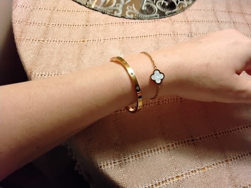 Customer's Vina Bracelet worn on a wrist alongside another gold bangle and a flower-shaped charm bracelet.