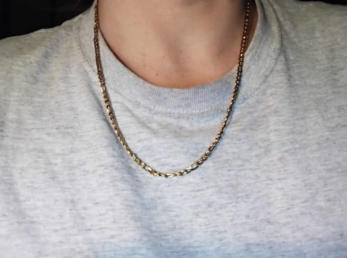 Customer's gold Positano Necklace worn around the neck against a grey shirt.