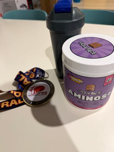 Customer's UGLYFACE AMINOS+ strawberry tub with a grey shaker bottle and IFBB competition medal on a white table.