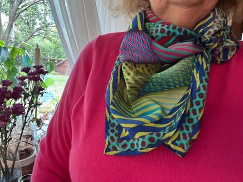 Customer's colourful Caroline Charles silk scarf tied around their neck, worn over a bright pink jumper.
