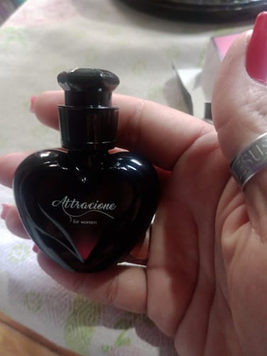 Customer's hand holding the heart-shaped black glass bottle of Perfume Attracione Sensual.