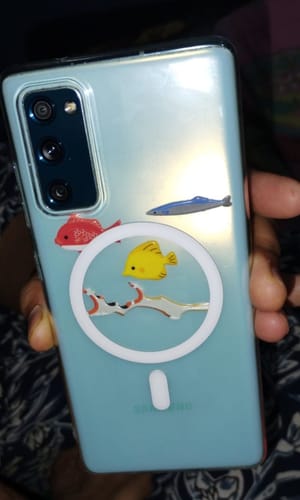 Customer's Anti Yellow MagSafe Clear Case on a light blue smartphone held in a hand, decorated with fish stickers.