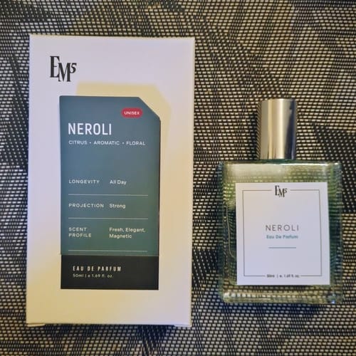 Customer's Neroli Eau De Parfum box beside the matching clear glass perfume bottle on a textured surface.