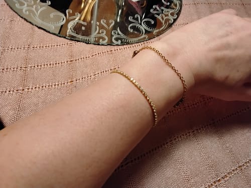 Customer's gold-toned Melly Adjustable Tennis Bracelet worn on a wrist alongside another simple gold chain bracelet.