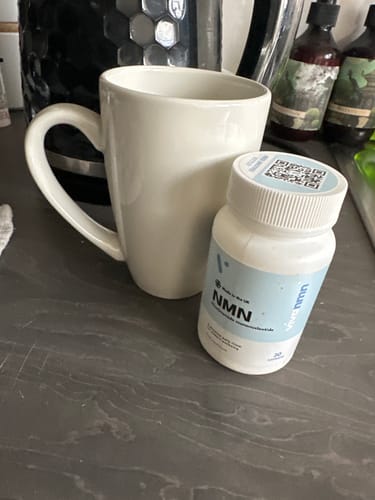 Flacon blanc de gélules Pure NMN de la cliente à côté d'une tasse blanche sur un plan de travail de cuisine gris.