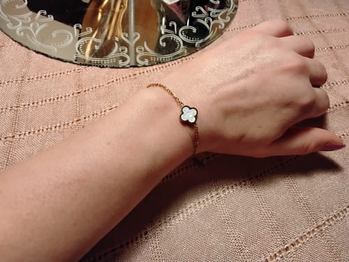 Customer's Nova bracelet with a gold chain and a white floral charm worn on a person's wrist.