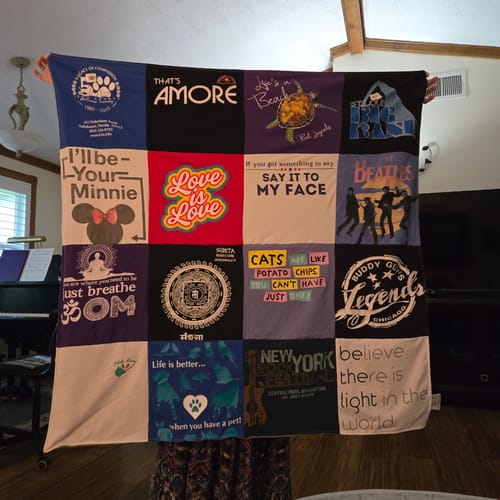 Reviewer's Project Repat T-Shirt Quilt held up, displaying a patchwork of various colorful t-shirt logos and designs.