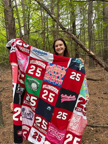 Customer's Project Repat T-Shirt Quilt featuring various red and black volleyball t-shirts, held up in a forest.
