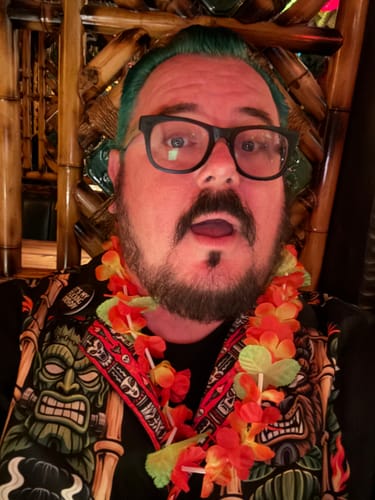 Customer's Monsters & Mai Tais Vintage Button Up shirt worn with a lei in a tiki bar setting.