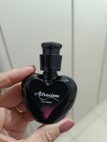 Customer's hand holding a heart-shaped black bottle of Attracione Sensual perfume.