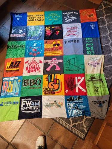 Customer's Project Repat T-Shirt Quilt laid out on a tile floor, featuring a colorful collection of race event shirts.