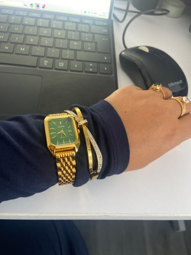 Customer's CLAIRE DE MAINS watch with a green face and gold band, worn on a hand at a desk with a computer mouse.