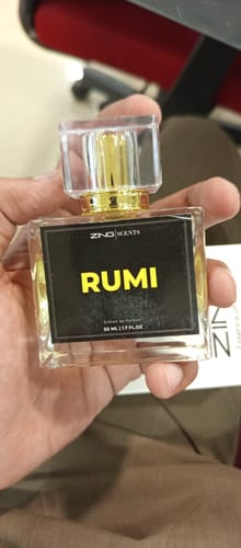 Customer's hand holding a square glass bottle of Rumi perfume with a gold cap.