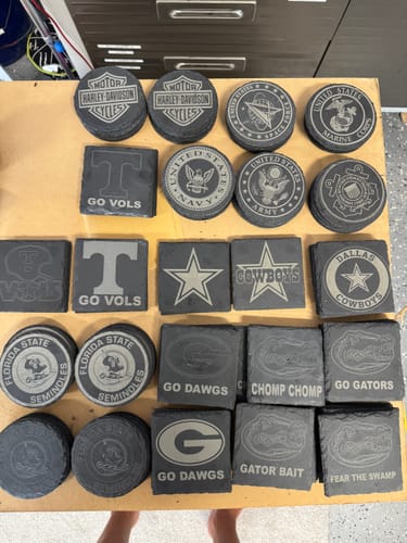 Reviewer's many slate coasters engraved with sports team logos using an AtomStack Swift laser engraver.