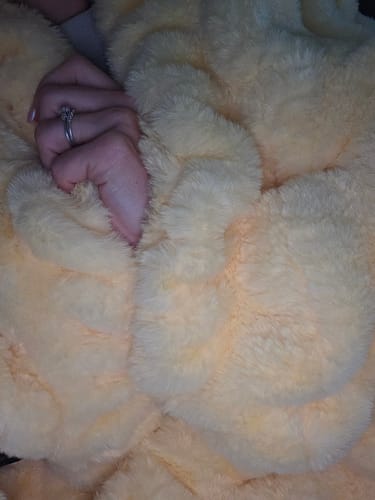 Customer's hand touching the plush, butter yellow Hugs Blanket to show its soft texture.