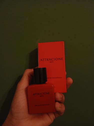Reviewer's hand holding the red Attracione Men perfume bottle with its matching box in the background.