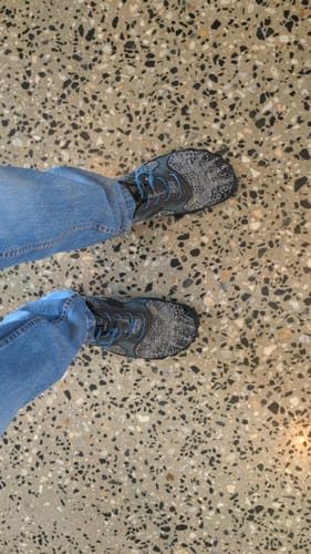 Customer's Fast Ⅰ barefoot shoes with blue laces, being worn with jeans on a speckled floor.