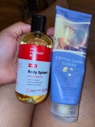 Reviewer's Yummy Body Splash hydrating oil held in hand next to a tube of body cream.