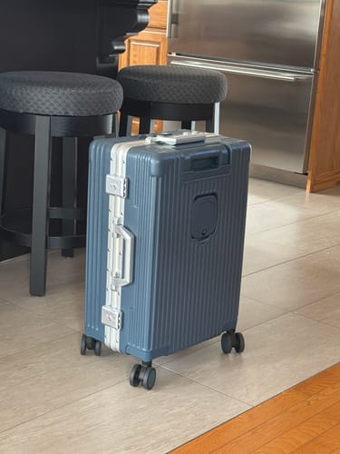 Customer's blue All-in-One Carry-On suitcase standing upright in a kitchen with stools in the background.