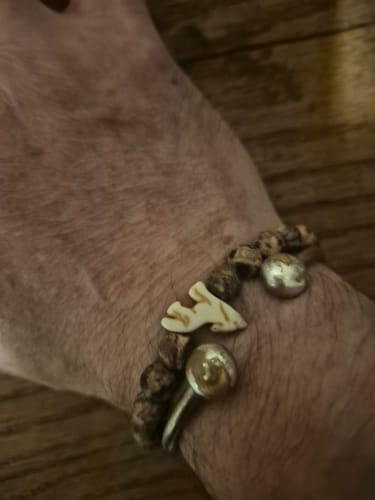 Customer's hand wearing The Scout Bracelet, featuring brown stone beads and a small light-colored wolf charm.