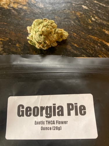Customer's Georgia Pie THCA Flower in a black pouch next to a dense, green cannabis bud.