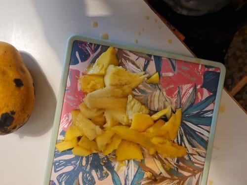Kundenfoto einer Mango Mingolo: eine ganze, dunkle Frucht neben einem Schneidebrett mit gelben, klein geschnittenen Stücken.