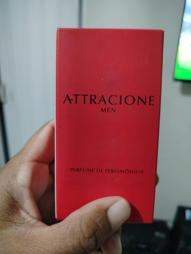 Customer's hand holding the rectangular red box of Attracione Men perfume with clear branding.