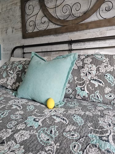 Customer's yellow Blem clitoral massager sitting on a gray patterned bedspread in a bedroom.