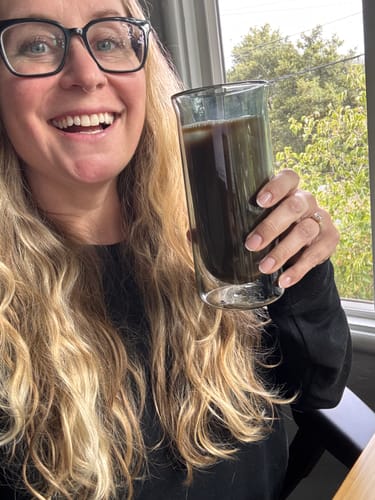 Customer's hand holding a filled FLUR iced coffee glass while smiling.