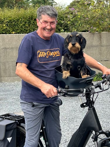 Customer's small black dog sitting comfortably in a dark Kvisp Dog Bike Carrier mounted to the bike handlebars.