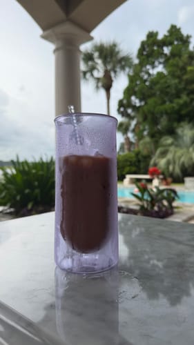 Customer's purple FLUR double-walled glass filled with ice coffee, sitting on a table outdoors near a pool.