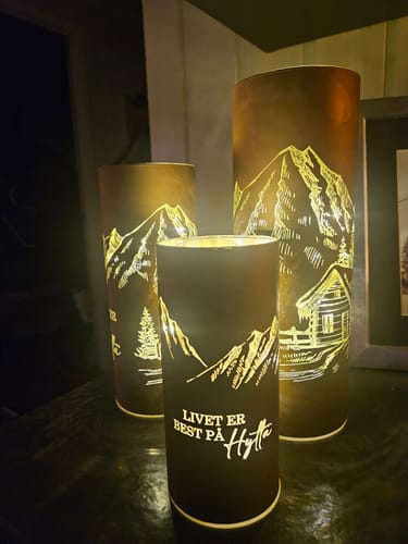 Customer's three brown Lyslykt LED-lykter med opplyste fjellmotiver og tekst plassert i et koselig mørkt rom.