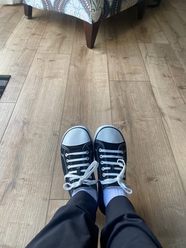 Customer's Roam I barefoot shoes in black and white on the person's feet, standing on a wooden floor.