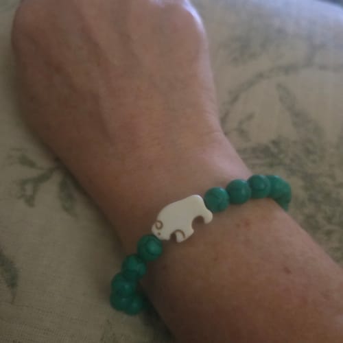 Customer's wrist wearing The Mystery Bracelet with turquoise-colored beads and a white animal-shaped charm.