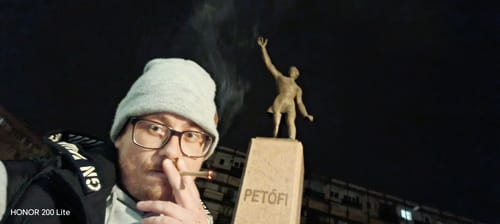 Reviewer's hand holding a lit Lemonatti THC-A flower pre-roll at night outdoors.