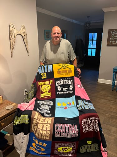 Customer's Project Repat T-Shirt Quilt held up by a person, featuring colorful blocks of various coaching jerseys.