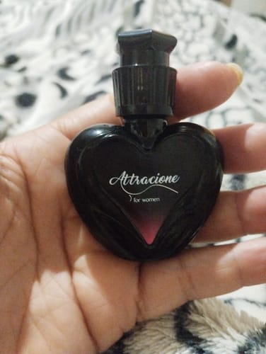 Customer's hand holding a small, heart-shaped black bottle of Attracione perfume.