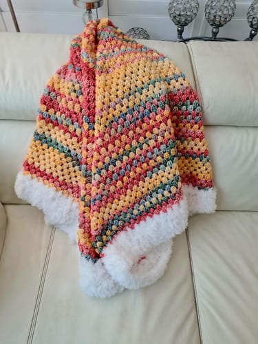 Customer's Rainbow Blanket Kit showing a finished blanket with colorful gradient yarn and a white faux-fur border