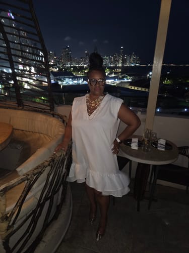 Reviewer wearing a white High-Low Loose Pleated Ruffled Mini Dress while standing on a terrace at night.